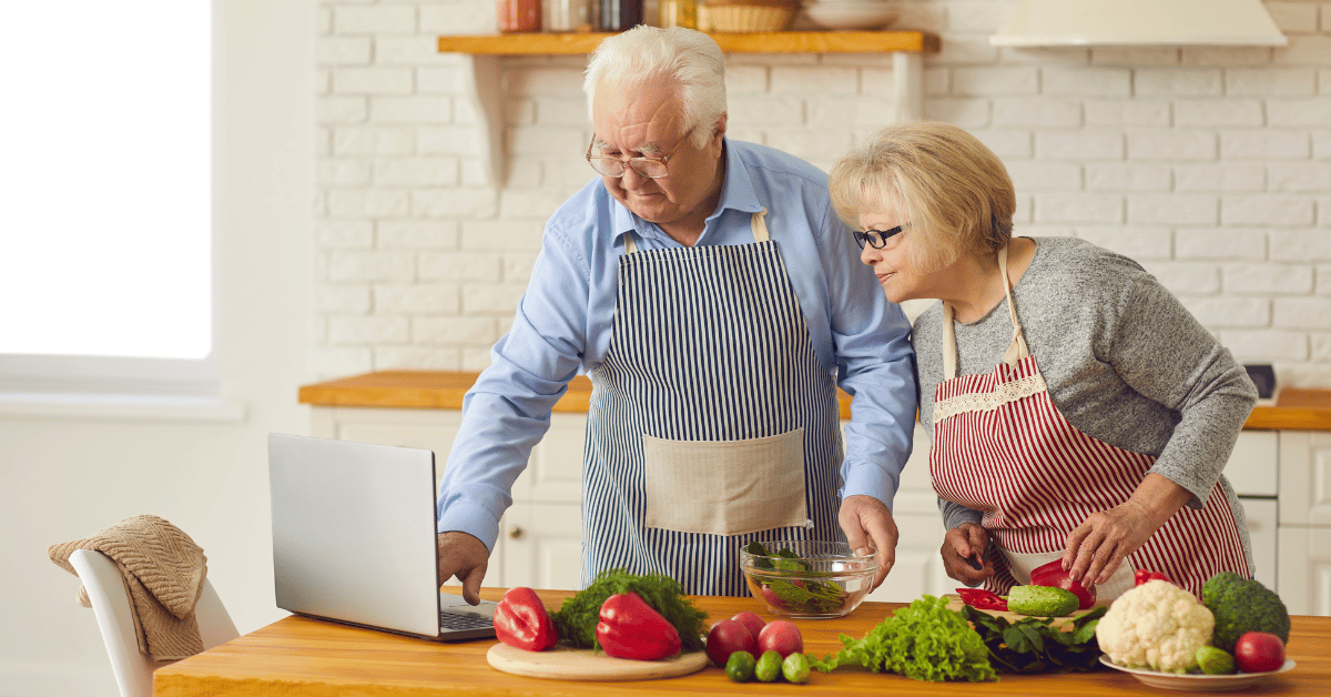 Pareja de ancianos cocinando alimentos sanos en la cocina mostrando cómo poner en práctica un envejecimiento saludable.